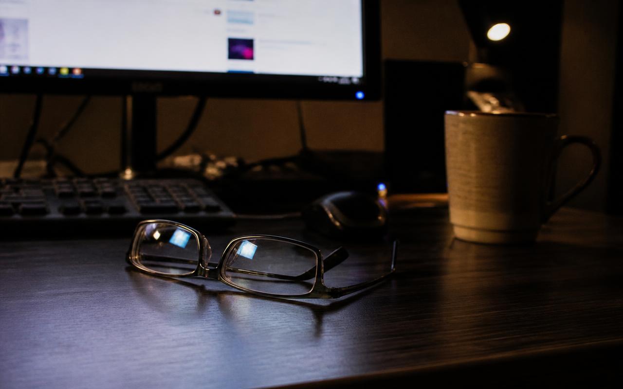 Óculos sobre a mesa em frente ao monitor aceso em um escritório à noite
